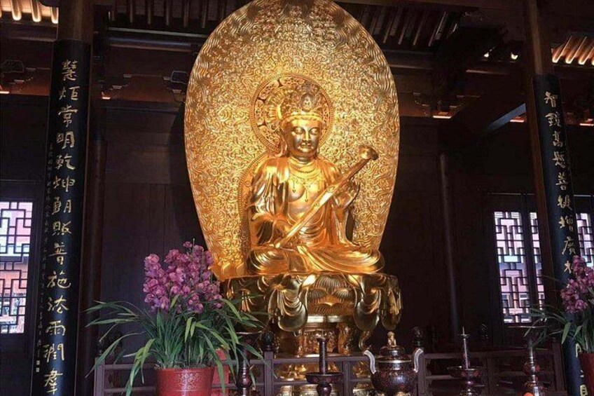 Eine goldene Buddha-Statue mit aufwendigen Mustern, umgeben von Topfpflanzen und traditioneller chinesischer Architektur. 4