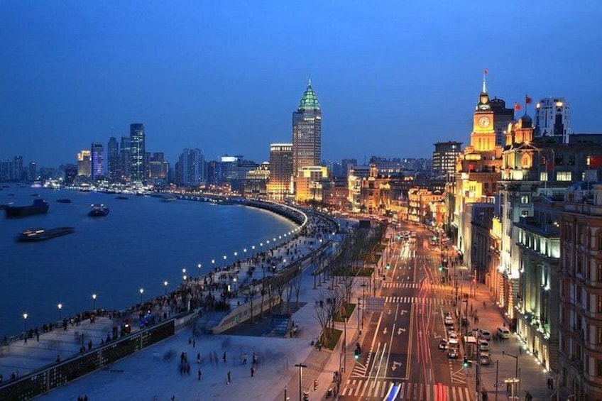 A coastal cityscape at dusk with illuminated buildings, a prominent clock tower, and a promenade along the waterfront. 2