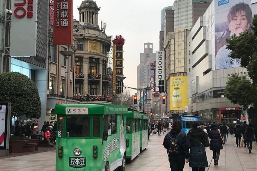 Ein grüner Bus auf einer Stadtstraße mit Fußgängern, Gebäuden und Werbetafeln. 2