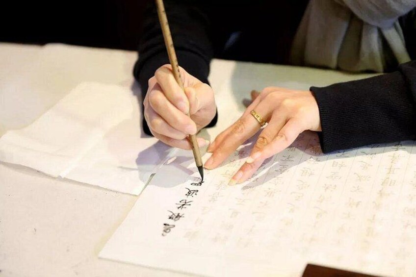 Una persona escribiendo caracteres chinos con un pincel sobre papel. 2