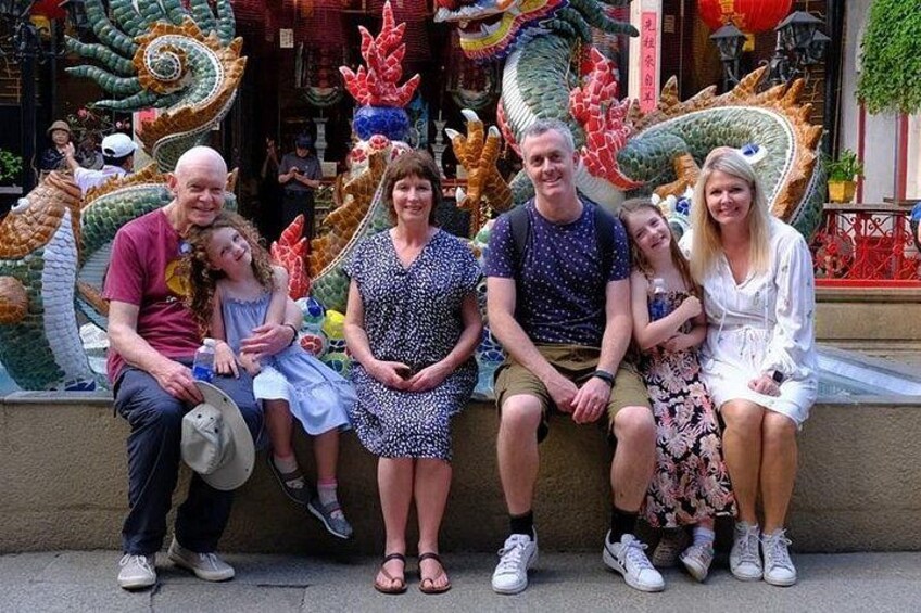 A group of people sitting on a ledge in front of a dragon sculpture. 4