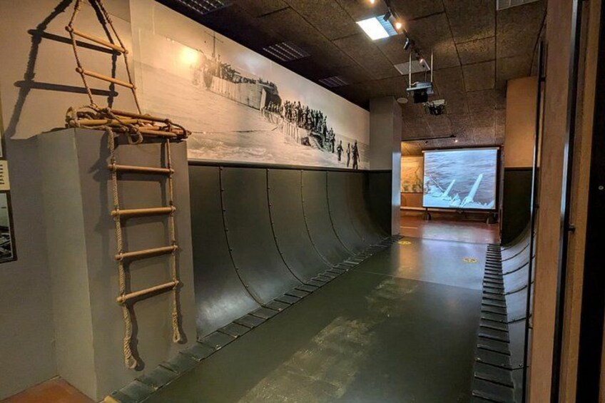 En udstilling på et museum med et stort muralmaleri, en rebstige og en buet væg. 3