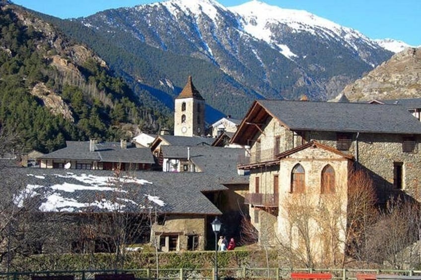 A mountain village with stone buildings, a church, and snow-capped mountains in the background. 1