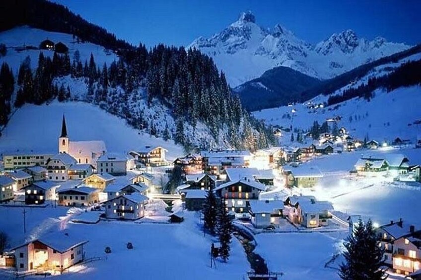 A snow-covered village with houses, a church, and mountains in the background. 1