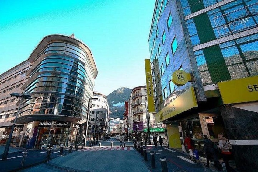 A city street with modern buildings, a pedestrian crossing, and a mountain in the background. 5