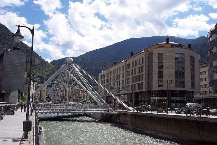 A bridge with a unique design, a river, and buildings in a mountainous area. 4