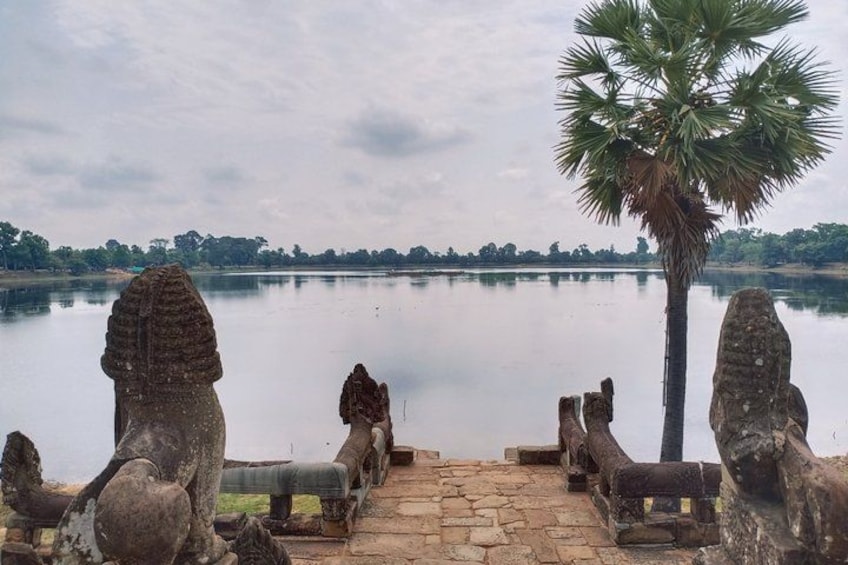 A stone pathway leading to a calm lake with palm trees and stone sculptures. 3
