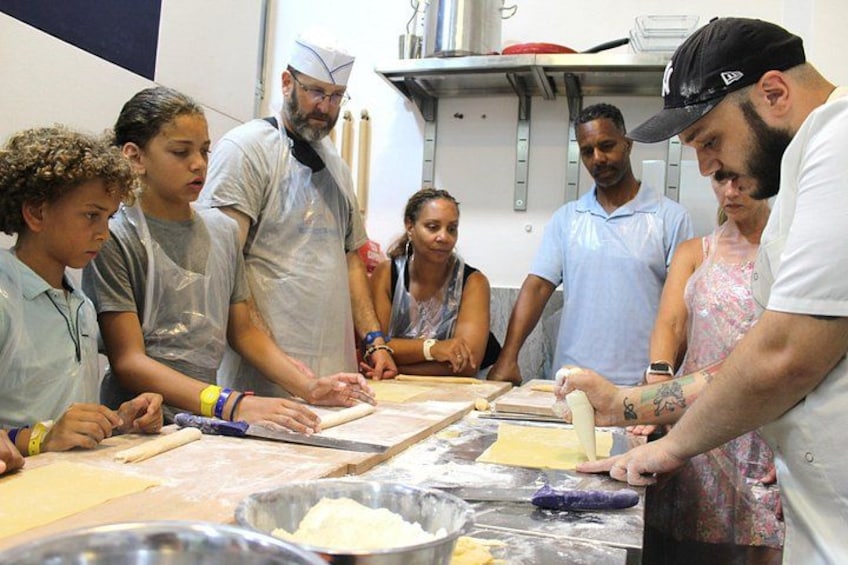 A group of people engaged in a cooking activity, using rolling pins and dough on a table. 1