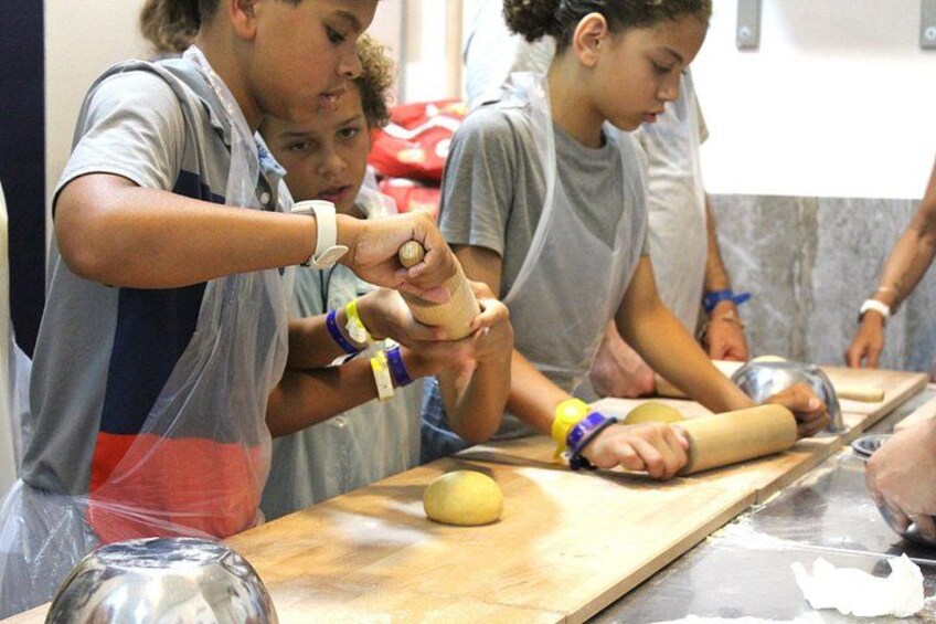 People engaged in a cooking activity, using wooden rolling pins and a rolling surface. 5