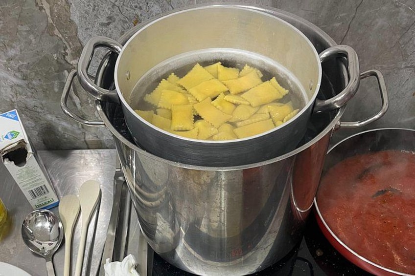 A stainless steel pot with handles on a stove, containing yellow food items, and a red pot on the right. 4