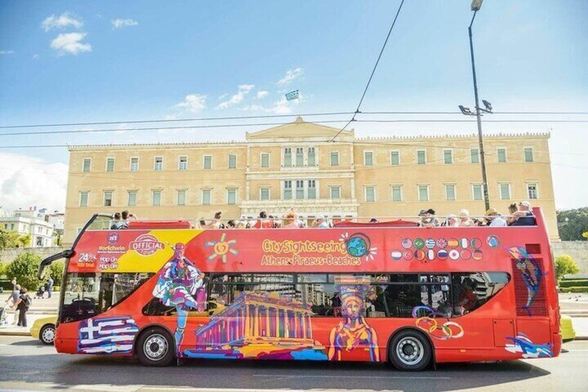 A red double-decker bus with colorful murals and advertisements, parked in front of a building. 5