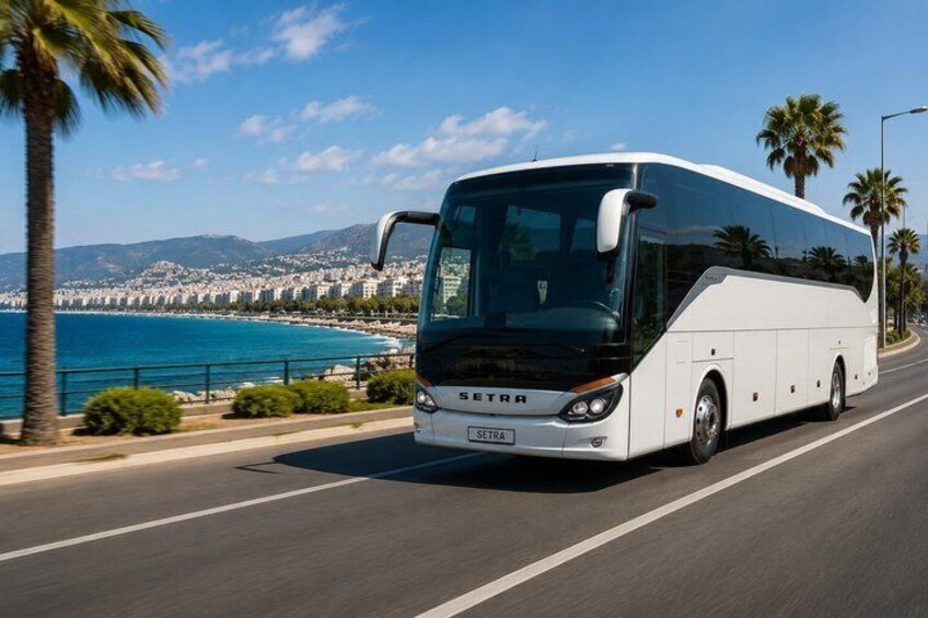 A white SETRA bus driving on a coastal road with palm trees and a clear blue sea in the background. 2