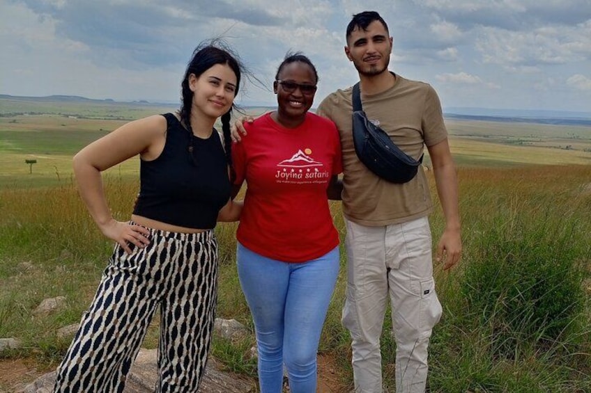 Three people standing on a grassy hill with a flat landscape in the background. 5