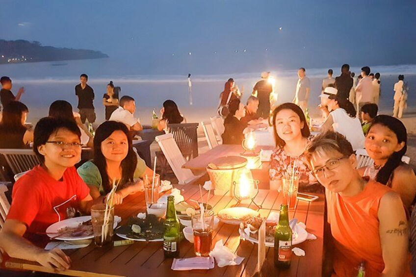 Un grupo de personas cenando en una mesa con vistas a la playa y al océano al atardecer. 5
