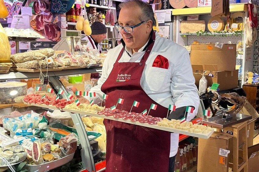 A person in a red apron holding a tray of various meats at a market. 4