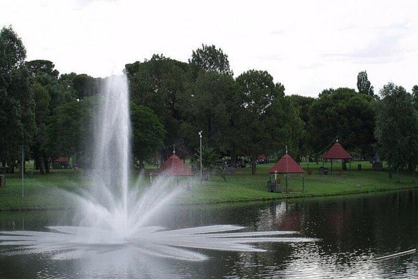 Een fontein in een park met bomen en gebouwen met rode daken. 5