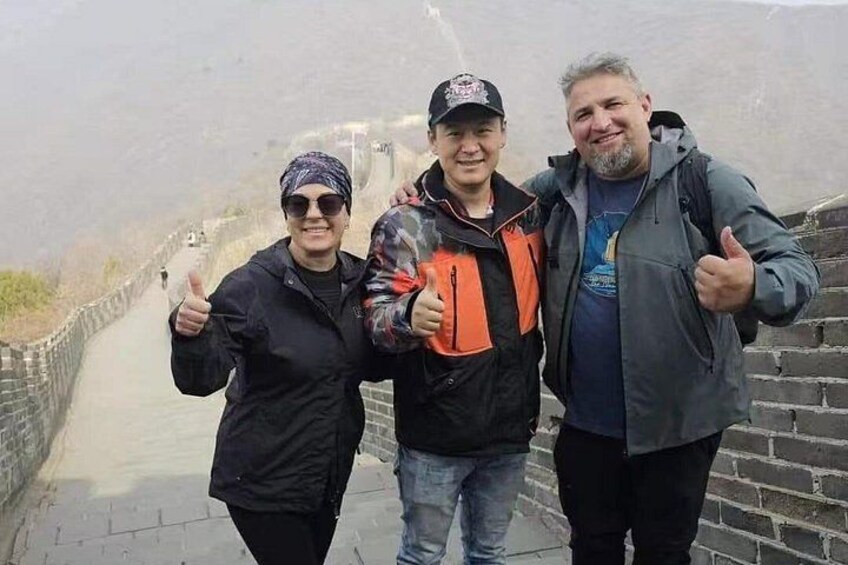 Three people standing on a historical wall with a mountainous landscape in the background. 1