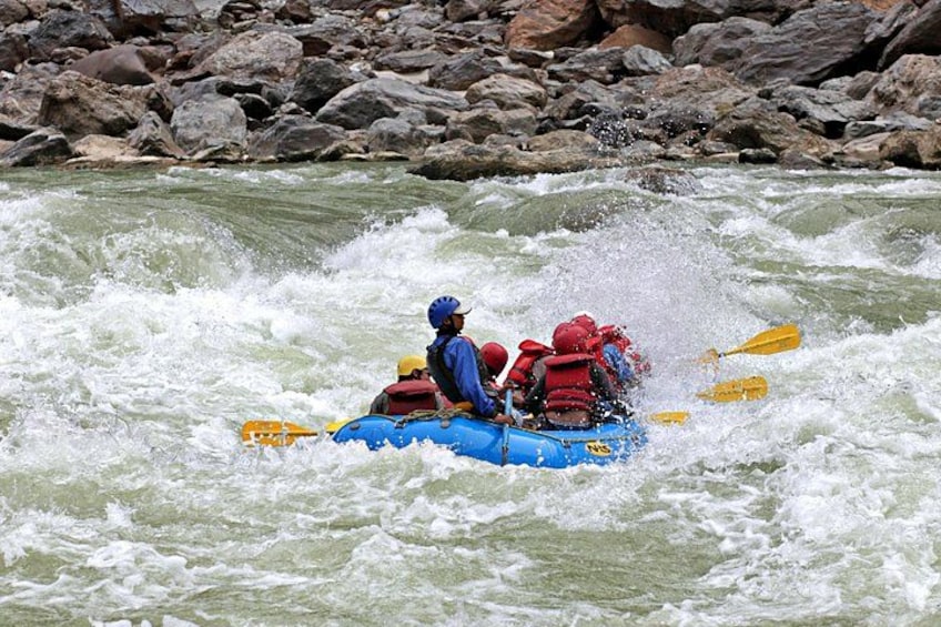 Un groupe de personnes à bord d’un radeau bleu navigue sur une rivière aux rapides tumultueux. 1