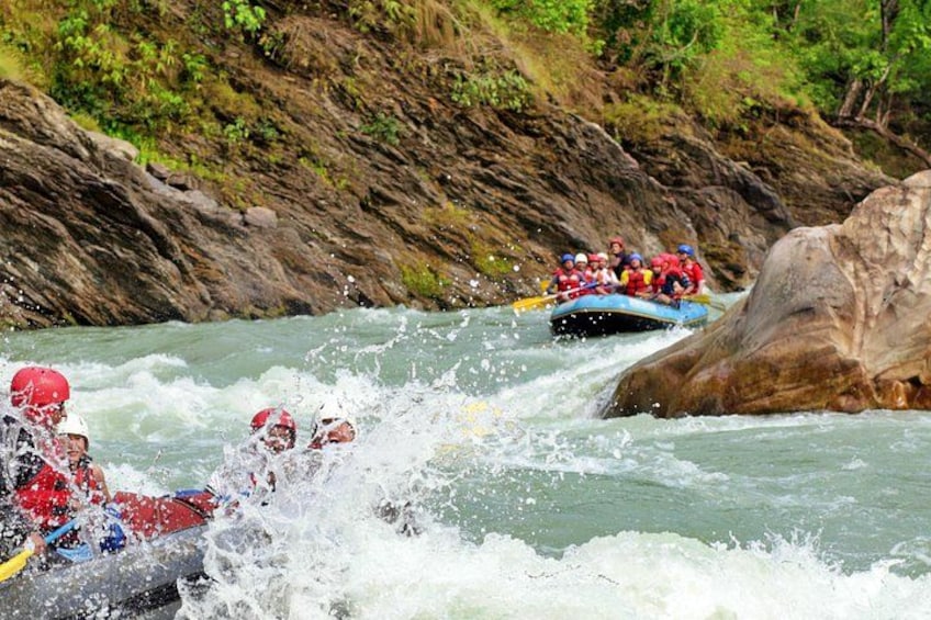 Un groupe de personnes fait du rafting sur une rivière à courant rapide, entouré d’un paysage rocheux et de végétation luxuriante. 3
