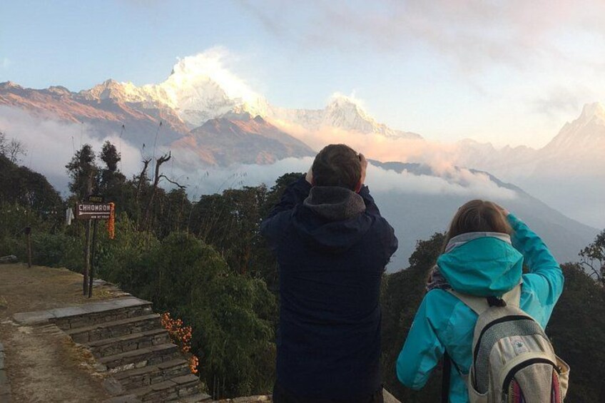 Two people hiking on a mountain trail with a view of snow-capped peaks and a sign indicating 'Chimboracito'. 4