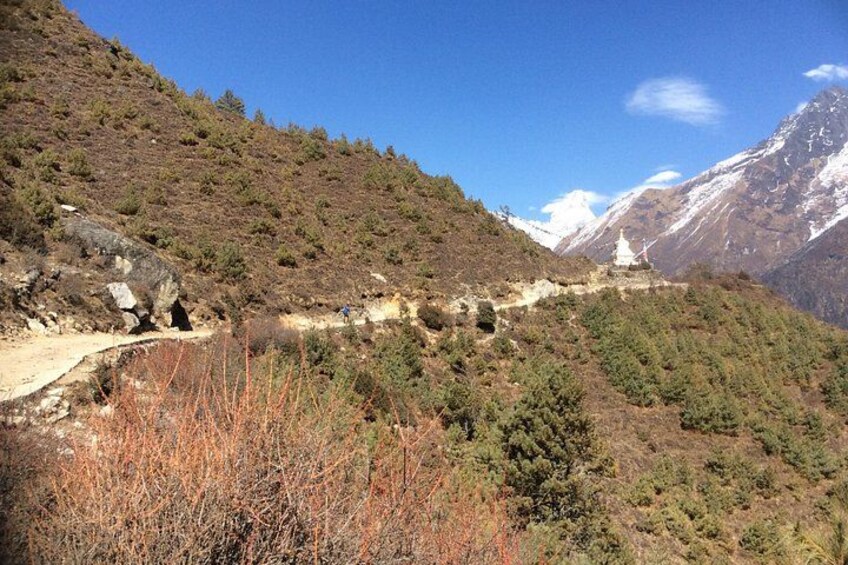 A mountainous landscape with a dirt path, sparse vegetation, and a distant snow-capped peak. 2