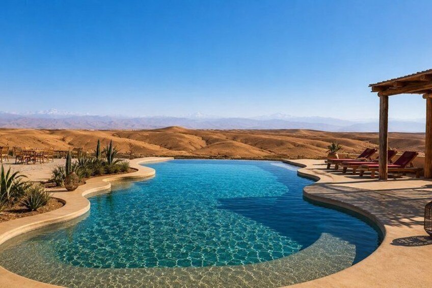 A clear blue pool with a curved edge, surrounded by desert landscape and a wooden pergola with lounge chairs. 2