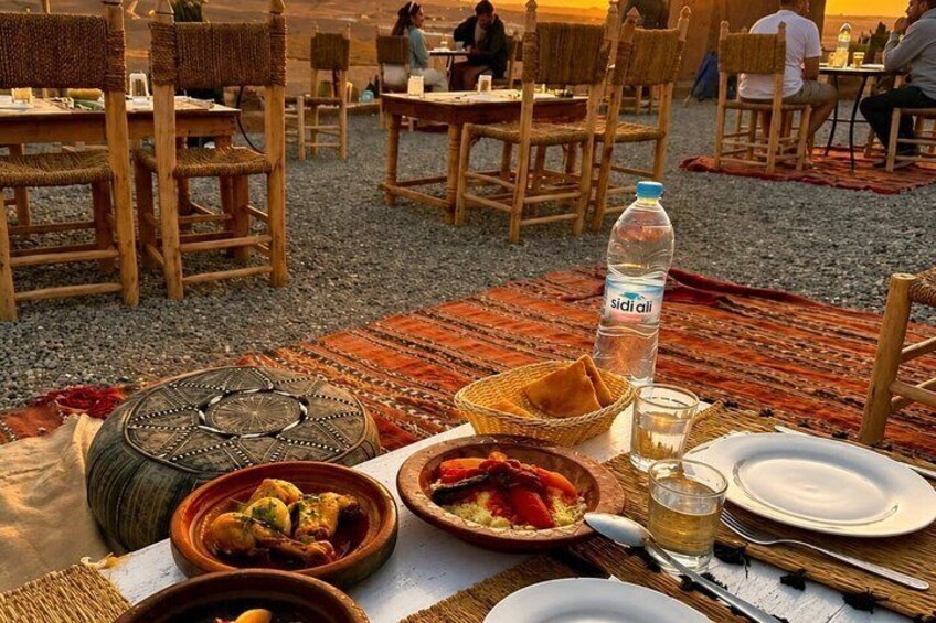 A dining setup with traditional woven chairs, a woven mat, and a table with food and drinks. 4