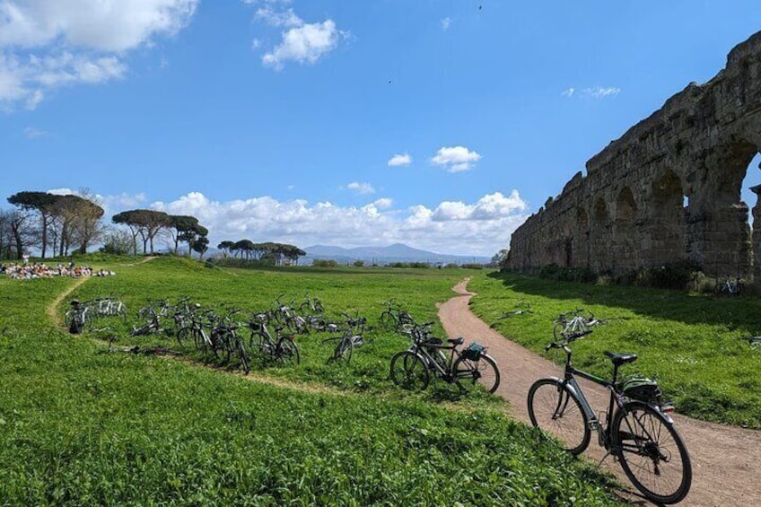 A pathway lined with bicycles, a stone structure, and a grassy field with trees. 1