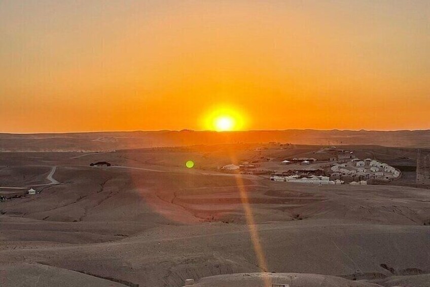 A desert landscape at sunset with a road, a small settlement, and distant hills. 4