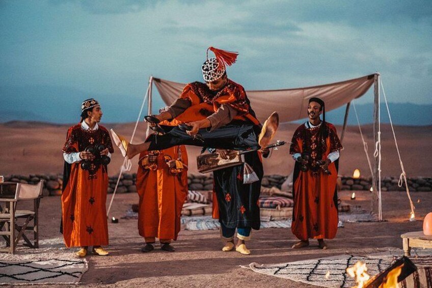 A desert scene with a group of people in traditional attire, a tent, and a campfire. 3