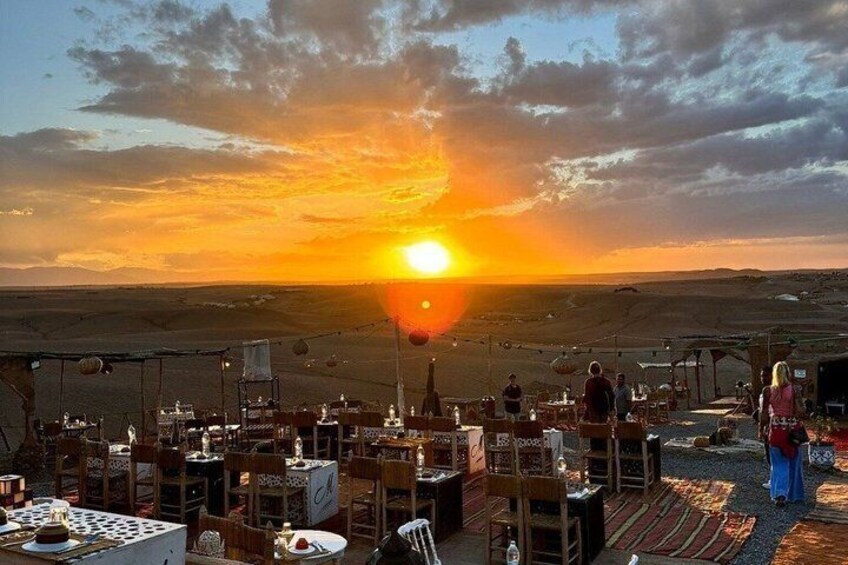 A sunset over a desert landscape with tables and chairs set up for dining. 2