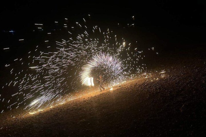 A person standing on a dirt path with sparks flying from a device, creating a light trail. 3