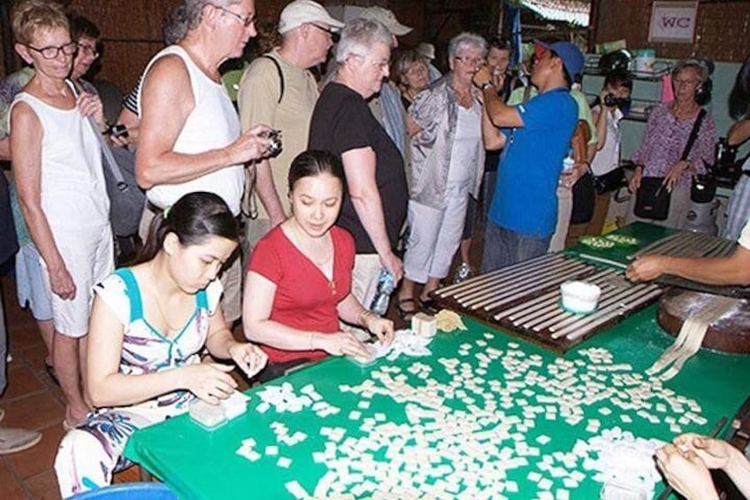 A group of people at a food stall with a green table, some cutting food items. 5