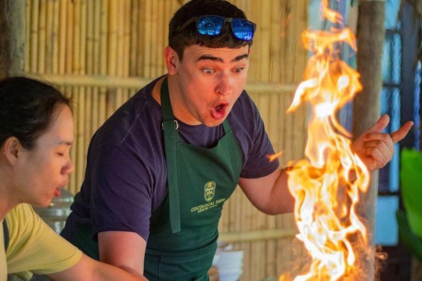 A person in a green apron with a logo, holding a torch with flames. 2