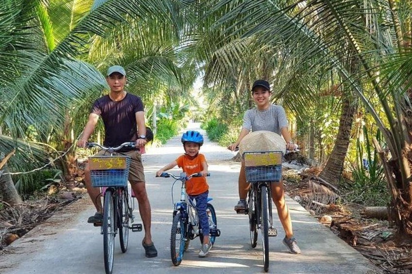 Three people on bicycles on a paved path surrounded by palm trees. 4