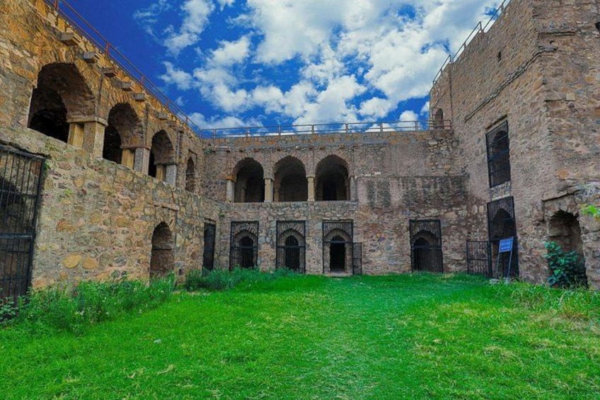 An ancient stone building with arched windows and a grassy courtyard. 2