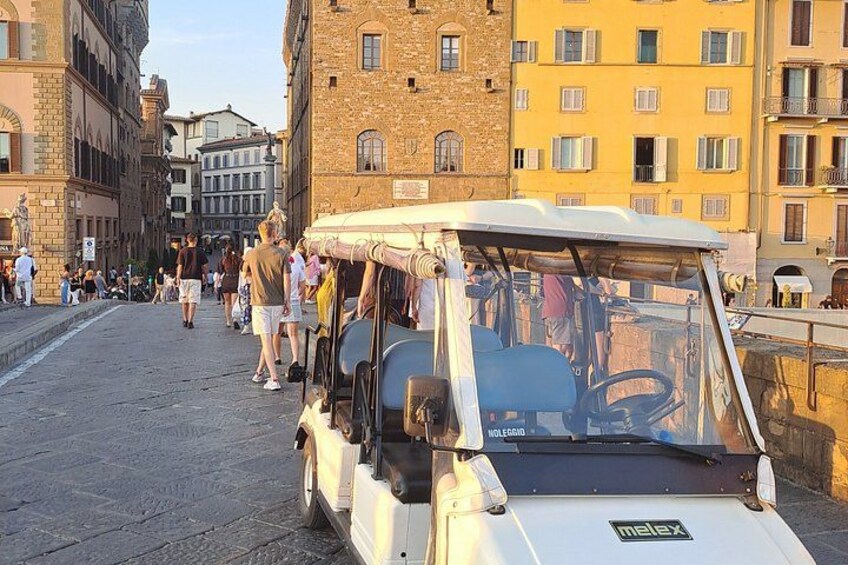A white golf cart parked on a cobblestone street with people walking in the background. 5