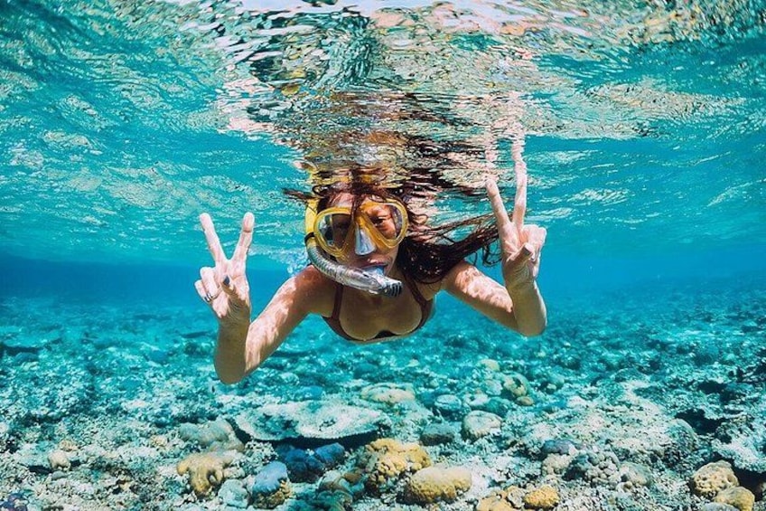Une personne sous l’eau, faisant un signe de la paix, entourée d’une eau d’un bleu limpide et d’un fond marin rocheux. 1