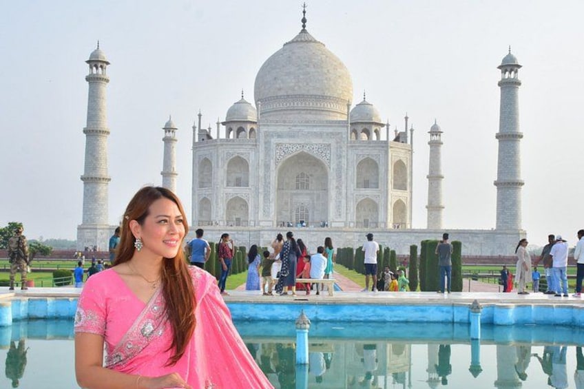 A person in pink attire standing in front of the Taj Mahal with a reflection in the water. 2