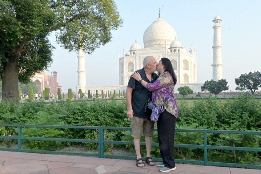 A couple kissing in front of the Taj Mahal with a tree and a fence in the foreground. 1