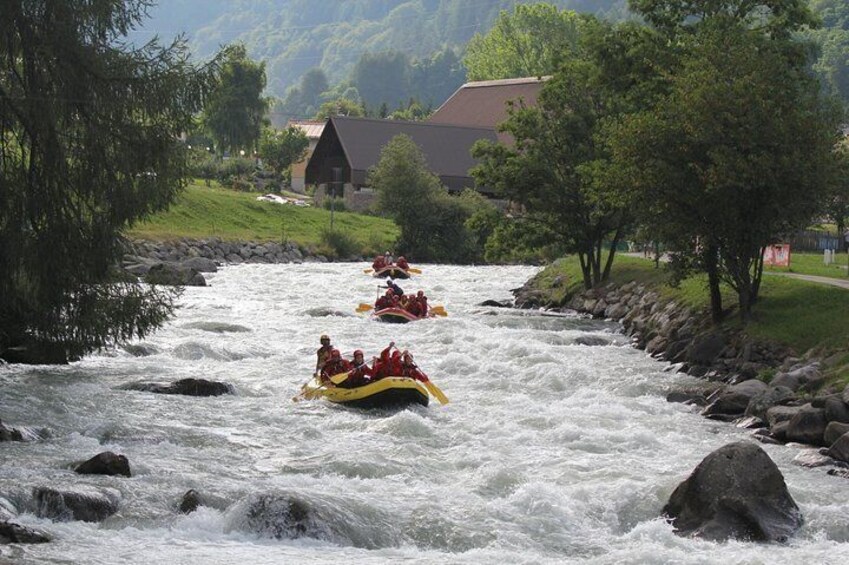 Menschen treiben auf Rafts einen reißenden Fluss hinunter, umgeben von Bäumen und einem Haus. 5