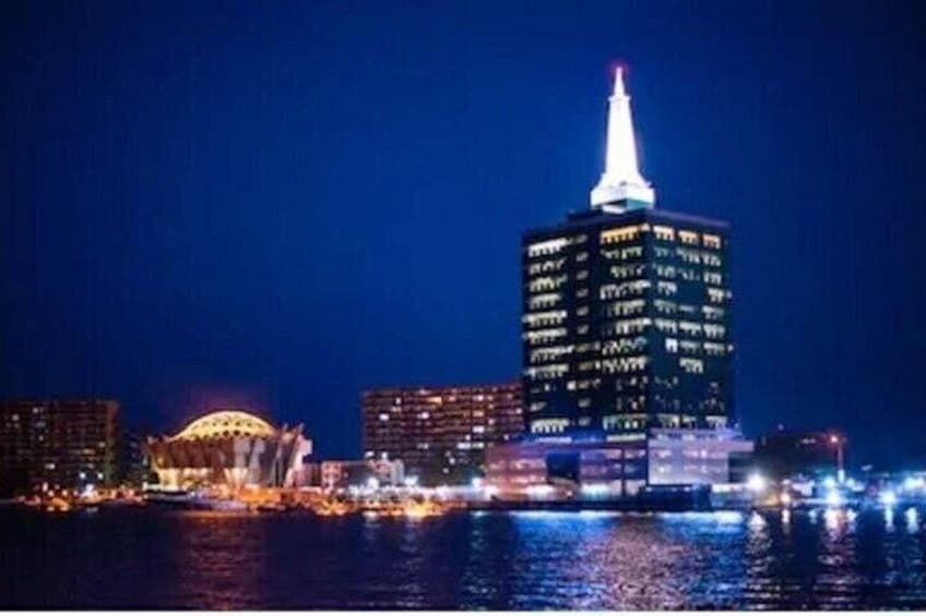 Une vue nocturne sur les gratte-ciel d’une ville, avec des bâtiments illuminés et une étendue d’eau au premier plan. 4