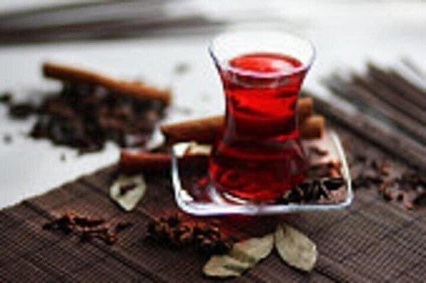A glass of red liquid on a square coaster, surrounded by scattered spices. 2