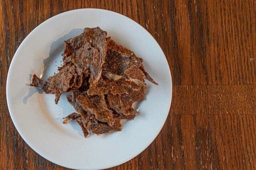 A white plate with dried meat pieces on a wooden table. 4