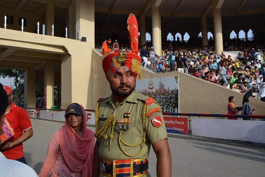 A military officer in uniform with medals, standing in front of a crowd at a public event. 2