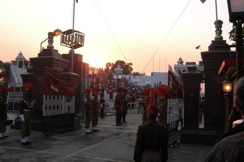 A ceremonial event with participants in traditional attire, a large gathering, and a prominent gate with a sign. 4