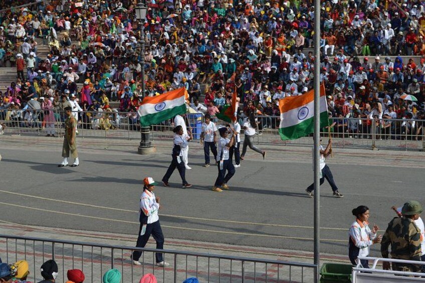 A parade with people holding flags, a crowd watching, and a road with barriers. 5