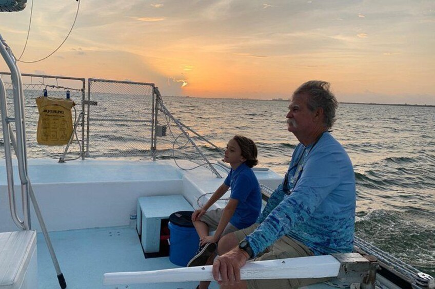 A boat with two people, one adult and one child, on a calm sea during sunset. 5