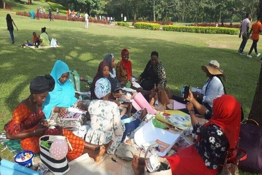 A group of people sitting on the grass in a park, some reading and others using their phones. 3