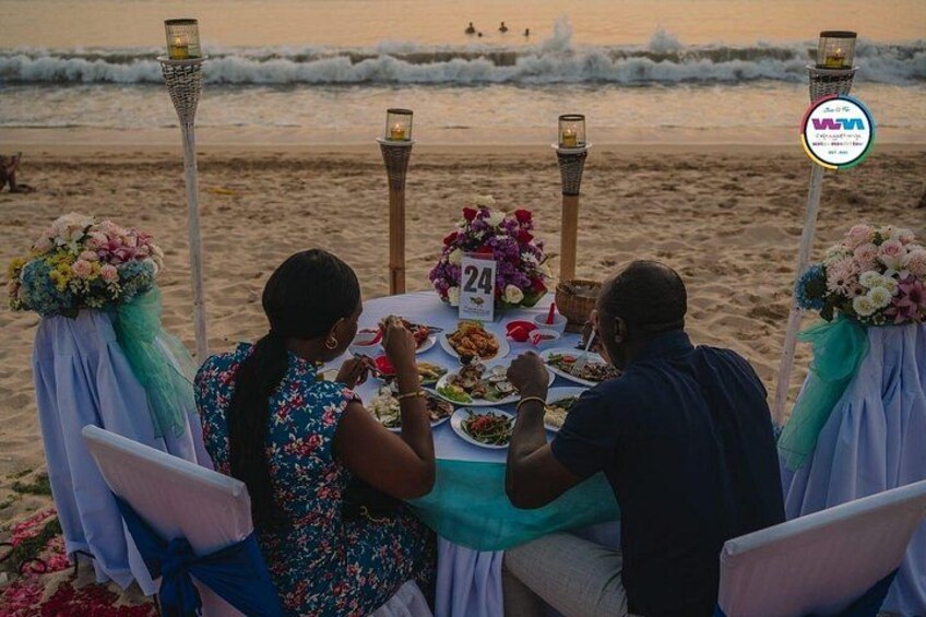 A beachside dining setup with a table, chairs, and decorative flowers. 2